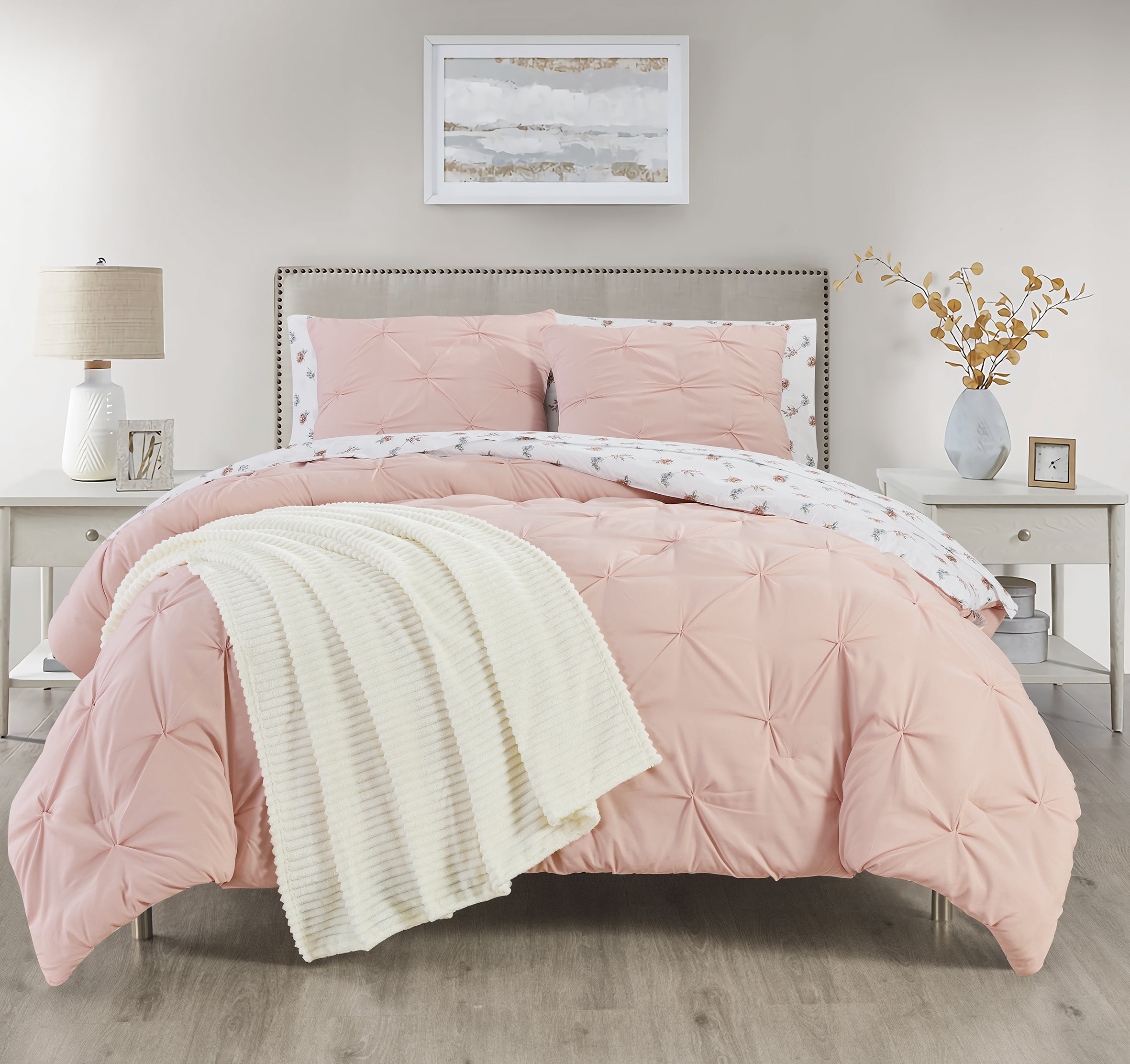 Pink comforter set on a bed in a bedroom with a lamp and framed picture in the background.