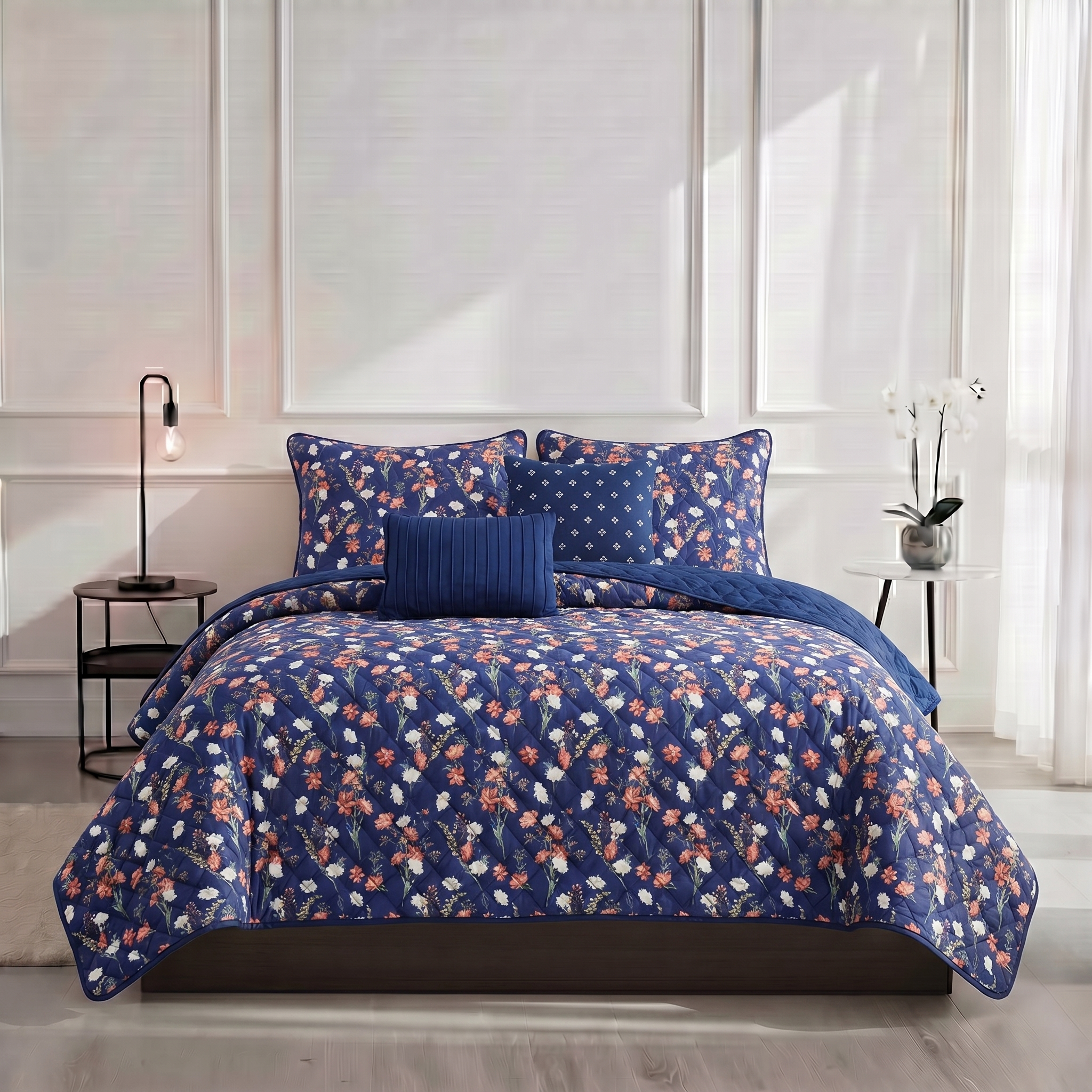 Blue floral bedding set on a bed in a bedroom with white walls and a lamp.
